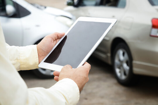 Auto insurance concept. A man, a company officer holding a tablet, takes pictures and records the accident car to inform the insurance company.
