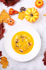 Pumpkin puree soup with shrimp and pumpkin seeds. Autumn menu for a restaurant or cafe. Photo on a light background.Small pumpkins and autumn leaves on a light background. Flat lay. Top view.