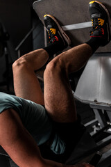 Slim Caucasian man training his legs on a gym machine. Man with blue sleeveless shirt and shorts training in a gym. High quality photo
