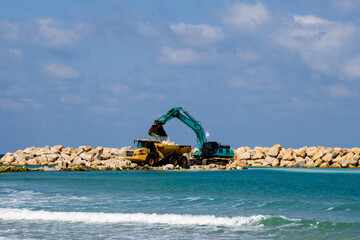 An excavator and a mining truck move stones into the sea. Construction of breakwaters to protect...