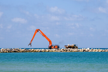 An excavator and a mining truck move stones into the sea. Construction of breakwaters to protect...