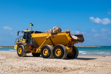 Fototapeta na wymiar A large mining truck transports stones to build breakwaters to protect a beach in Netanya, Israel.