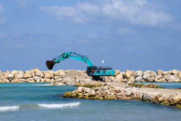 The excavator moves stones into the sea. Construction of breakwaters to protect the beach in...
