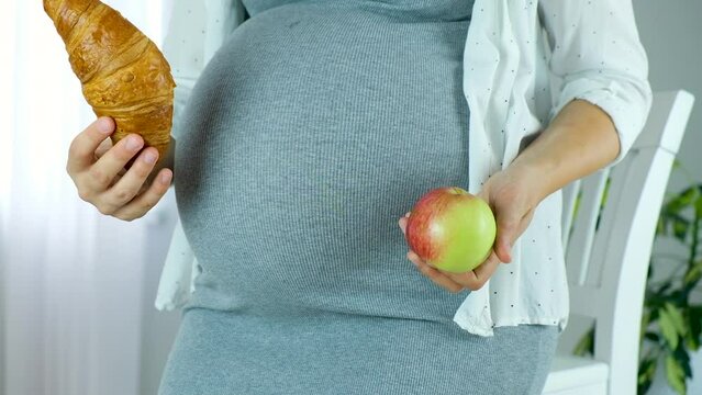 Pregnant woman choose croissant or fresh apple fruit think about what to eat. The concept of healthy and unhealthy food during pregnancy. Cravings of dessert and pastry while carrying child.