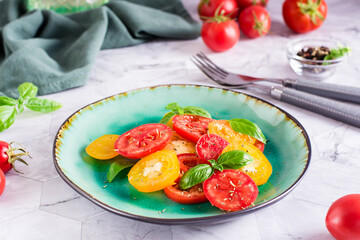 Sliced red and yellow tomatoes and basil leaves on a plate on the table