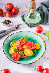 Fresh salad of yellow and red tomatoes with basil leaves on a plate on the table. Vertical view