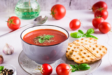 Fresh tomato soup with basil in a bowl and fresh vegetables on the table