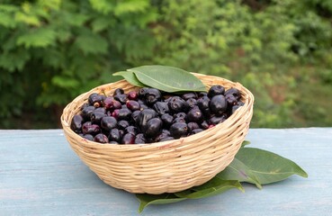 Jamun or Syzygium Cumini Fruit with Leaves in a Bamboo Basket on Wooden Background, Also Known as Java Plum, Malabar Plum, Black Plum or Jambolan