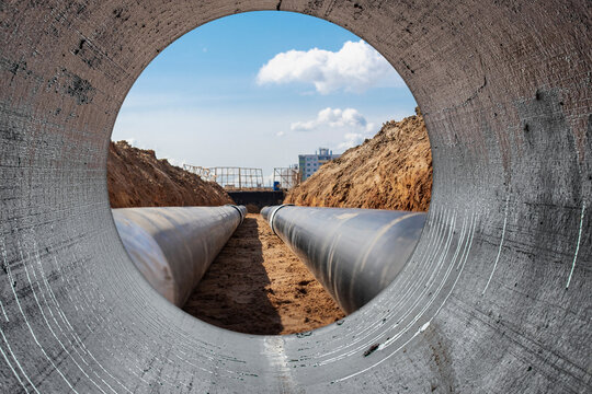 Water pipes for drinking water supply lie on the construction site. View from a large concrete pipe. Preparation for earthworks for laying an underground pipeline. Modern water supply systems.