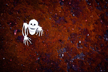 White plastic figurine skull-ghost with bones in the red moss background