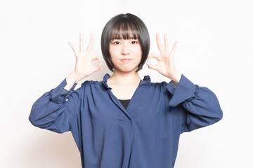白背景の前でOKのポーズをする若い女性
