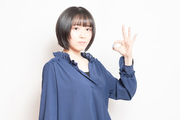 白背景の前でOKのポーズをする若い女性