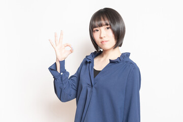 白背景の前でOKのポーズをする若い女性