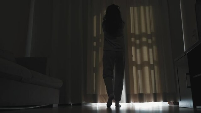 Happy young woman opens the curtains and looks out the window. Beautiful brunette opens the curtains to let the morning sunlight