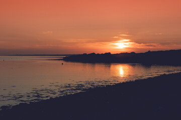 Fototapeta premium Sunset nature scene by the ocean. Silhouette of the ocean coast. Warm orange color.