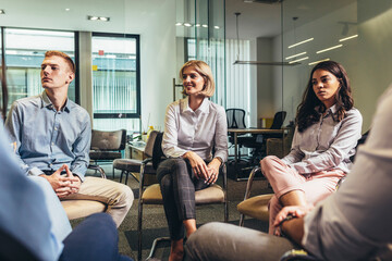 Group of people sitting in a circle on group therapy. Looking at their therapist and listening to her story.