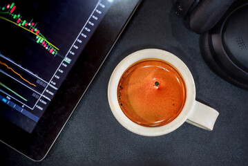 A Cup of Espresso Shot Coffee with a tablet show technical graph of Stock or crypto market