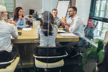 Office colleagues having discussion during meeting in conference room. Group of men and women sitting in conference room and smiling.