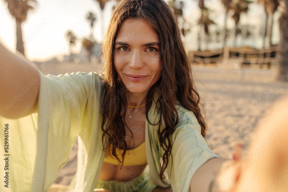 Wall mural image of young beautiful woman doing selfie and loot at camera. caucasian lady with long curly hair,