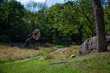 A young girl, with long blond hair, enjoying the beautiful summer day on a swing hanging by a long rope from an oak tree. A warm day on the island of Tjome in the fjord of Oslo, Norway.
