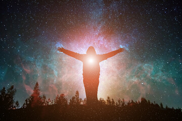 silhouette of young woman with outstretched arms  on top of forest mountain looking at the universe...