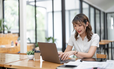 Cheerful young female businesswoman or student smiling and working on computer laptop at office.