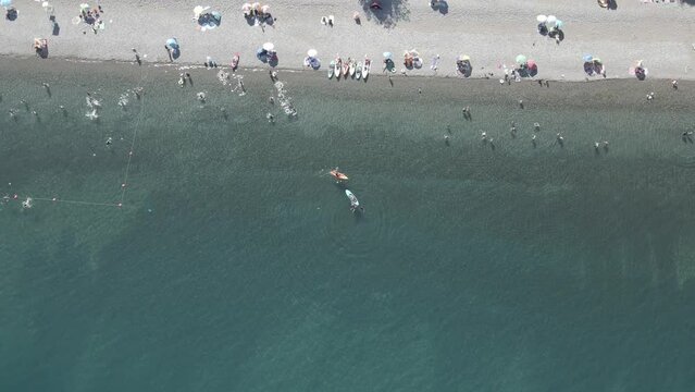 Aerial circling shot of  people bathing in the Ranco lake in Chile while there are people practicing paddleboarding 