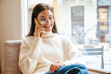 White brunette woman smiling and talking on mobile phone in cafe