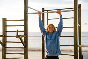 Young blonde man doing exercise while working out on horizontal bar