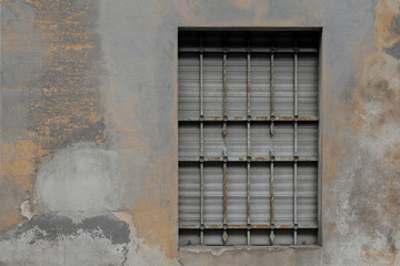 Old weathered stone wall with window, silver closed jalousie and bars in front of the frame