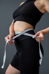  standing fitness woman measuring her waist with a tape with numbers.