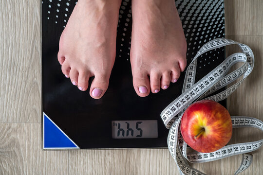  woman's legs standing on scales and a tape measure and an apple nearby in the middle hall.