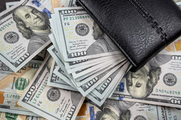 many dollars put in black wallet isolated on black background.