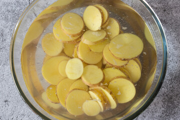 Sliced potatoes soaking, in a glass bowl, in water for cleaning. On a concrete background