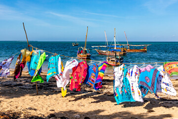 Sansibar, Dhow-Boote am Strand im Dorf Fumba auf Sansibar in Tansania. Im Vordergrund bunte Tücher.