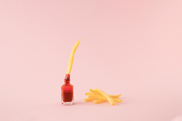French fried potato dipped in red nail polish with a pile of fries on the side on pink background. Minimal concept.