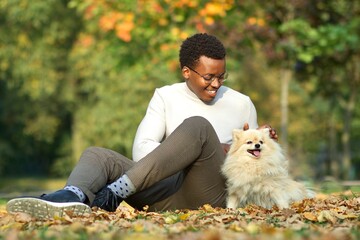Happy positive black African Afro American guy, young man owner sitting on ground with foliage,...