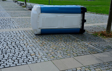 blue white plastic mobile toilet lying on its side. Overturned thanks to vandalism, drunkards,...