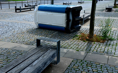 blue white plastic mobile toilet lying on its side. Overturned thanks to vandalism, drunkards, football hooligan rioters. square by the park, publicly accessible chemical toilet out of order , tree