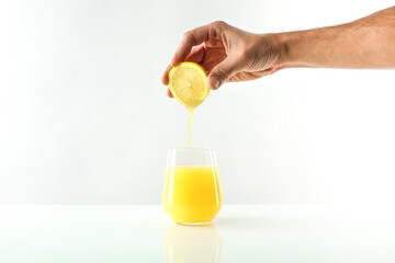 concept of freshly squeezed juice. hand squeezes juice from lemon into a glass. juice flowing into...