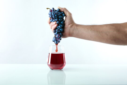 concept of freshly squeezed juice. hand squeezes juice from grapes into a glass. juice flowing into a glass on white background