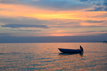 Silhouette of a boat near the shore against the background of the setting orange sun