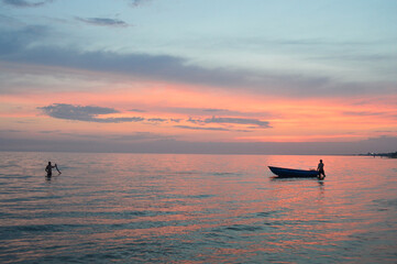 Fototapeta premium Silhouette of a boat near the shore against the background of the setting orange sun