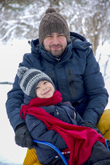 Father and son sledding in the snow in winter. Winter entertainment and recreation. The man and child are smiling into the frame. Warm clothes winter season