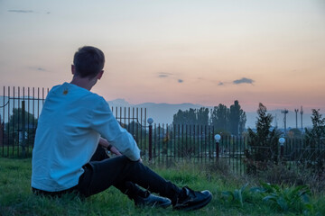 Fototapeta premium The guy sits on the grass admiring the sunset
