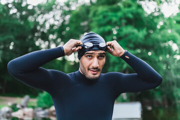 Man wearing wetsuit adjusting swimming goggles