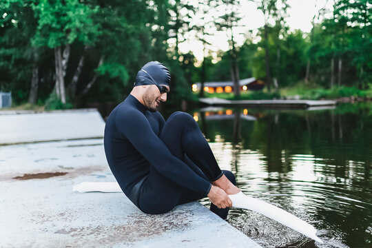 Man putting on diving flippers sitting by lake - Powered by Adobe