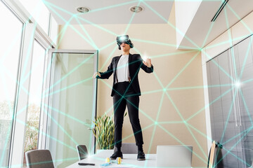 Businesswoman wearing virtual reality simulator standing on table in office