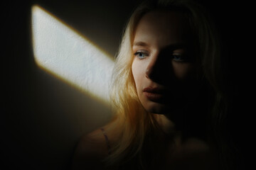 Sad young woman sitting in front of wall by rays of sunlight