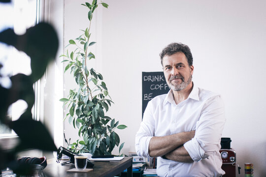 Confident Businessman With Arms Crossed At Office Coffee Corner